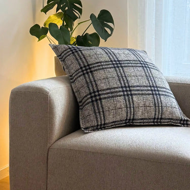 Coco prydnadskudde placerad i soffa, i rutigt möbeltyg som skapar en varm och ombonad inredning