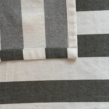 Närbild på fållen på en randig bordsduk i bomull som visar tygets struktur och sydda kant.