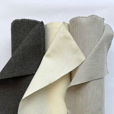 Tre rullar av ljushärdig uteväv i naturtoner där tyget är uppvikt för att visa struktur och väv. Slitstarkt tyg som passar för gardiner, dynor och andra utomhustextilier.