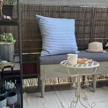 Ljusblårandig kudde i uteväv placerad på stol utomhus, slitstarkt och vattenavvisande tyg.