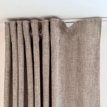 Beige gardin i linneliknande tyg med mjuka veck och synlig struktur, upphängd på gardinskena i tak.