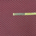 Närbild av möbeltyget Romeo i vinröd nyans med små prickigt geometriskt mönster och måttband som visar mönstrets storlek. Dubbelvävt tyg i 50 % polyester och 50 % bomull.