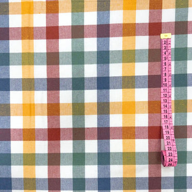 Närbild på rutigt tyg Ruth med rosa måttband som visar rutornas storlek. Återvunnet bomulls- och polyestertyg i gröna, gula, blå och röda toner.