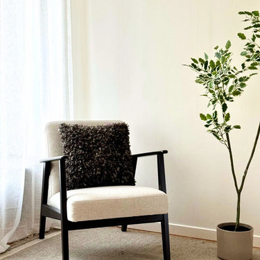 Svart kuddfodral 45x45 i fårskinnsimitation på fåtölj i vardagsrum