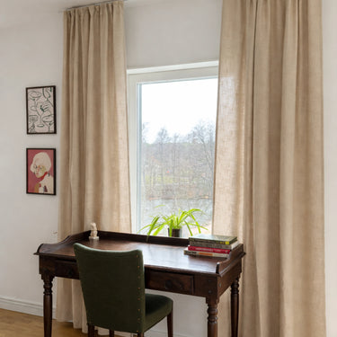 Beige gardiner i linnelook upphängda i vardagsrum med skrivbord och stol, mjukt ljusinsläpp