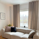 Beige gardinlängder i linnelook upphängda vid stort fönster bakom soffa, släpper in mjukt dagsljus