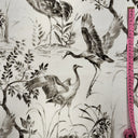 Ljust mönstrat tyg Cordelia i 100 % bomull med illustrerade tranor, träd och växter i mjuka grå och beige toner, fotograferat plant med måttband för skala.