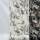 Mörkt mönstrat tyg Cordelia i 100 % bomull med tranor, bladverk och naturmotiv i beige och ljusa toner mot mörk botten, fotograferat plant för att visa mönster och kontrast.