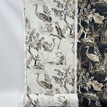 Mörkt mönstrat tyg Cordelia i 100 % bomull med tranor, bladverk och naturmotiv i beige och ljusa toner mot mörk botten, fotograferat plant för att visa mönster och kontrast.