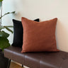 Enfärgat kuddfodral i brun-orange färg placerat på bänk med andra kuddar