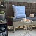 Ljusblårandig kudde i uteväv placerad på stol utomhus, slitstarkt och vattenavvisande tyg.