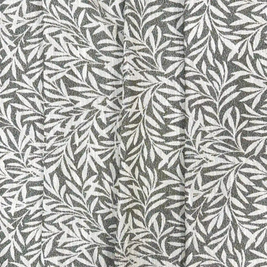 Närbild av möbeltyget Masra i grön färg med dekorativt växtmönster och tydlig vävd struktur. Slitstarkt tyg med 28 000 Martindale för möbler och inredning.