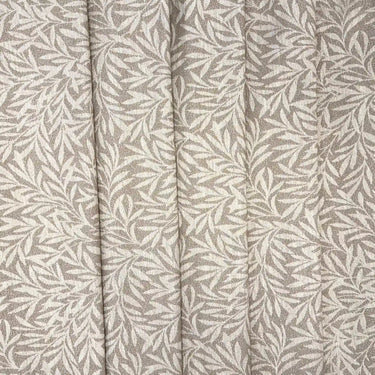 Masra möbeltyg i beige nyans med dekorativt bladmönster, fotograferat i mjuka veck som visar tygets fall och struktur. Slitstarkt tyg för möbler.