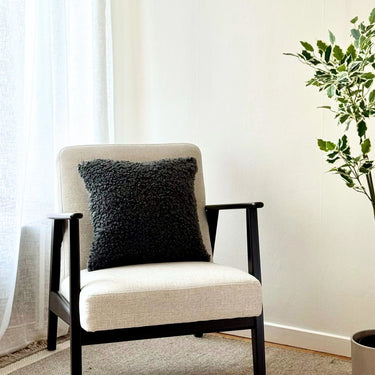 Svart kuddfodral 45x45 i fårskinnsimitation på fåtölj i vardagsrum