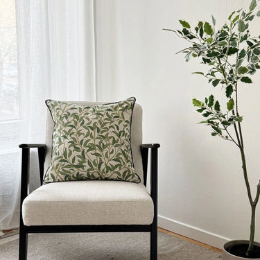 Olivia prydnadskudde placerad i fåtölj, med grönt bladmönster som skapar en mjuk och naturlig känsla i rummet