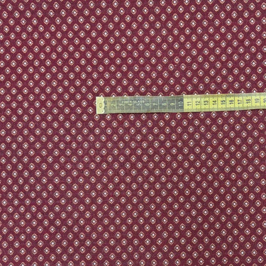 Närbild av möbeltyget Romeo i vinröd nyans med små prickigt geometriskt mönster och måttband som visar mönstrets storlek. Dubbelvävt tyg i 50 % polyester och 50 % bomull.