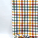 Rutigt tyg i grönt, gult, blått och vinrött hänger mot ljus bakgrund. Tyg i 80 % återvunnen bomull och 20 % återvunnen polyester med mjuk känsla och klassisk design.