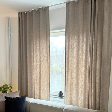 Närbild på beige gardintyg med linneliknande struktur och naturligt ljus som passerar genom tyget