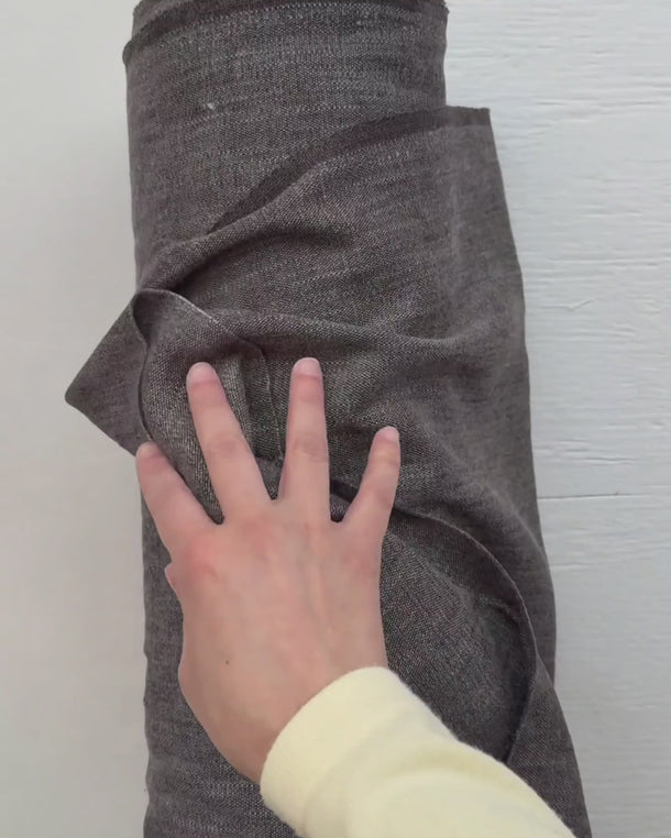 Hand som känner på möbeltyget Nova och visar tygets struktur och fall – slitstarkt tyg med 45 000 Martindale som passar möbler, gardiner och kuddar.