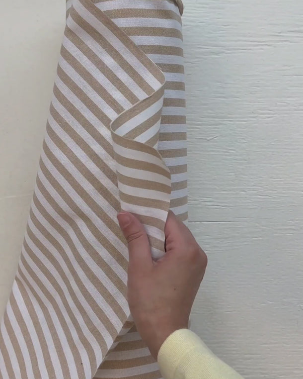 Hand som visar strukturen på den randiga uteväven Marina för dynor och utomhustextilier.