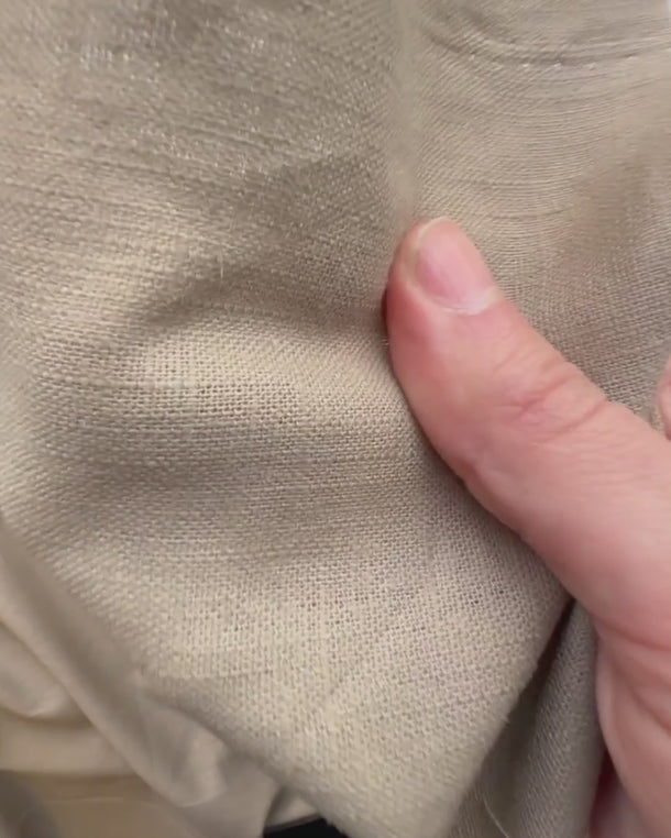 Hand som visar strukturen i gardintyget Ludwig – mjukt linne/bomull som faller naturligt