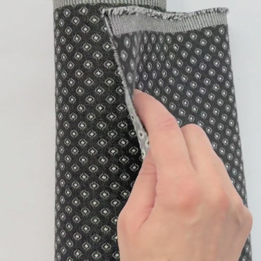 Video på mörkt möbeltyg Romeo med små geometriska mönster. Hand visar tygets struktur, väv och tjocklek – slitstarkt tyg för möbelomklädsel.