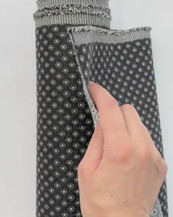 Video på mörkt möbeltyg Romeo med små geometriska mönster. Hand visar tygets struktur, väv och tjocklek – slitstarkt tyg för möbelomklädsel.