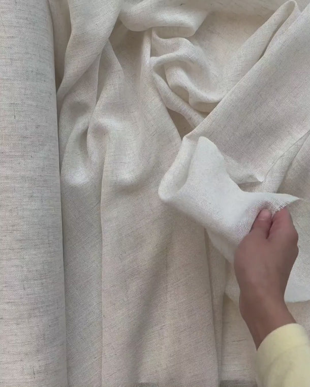 Hand som visar fallet i gardintyget Lova i linnelook och hur det luftiga tyget draperas.