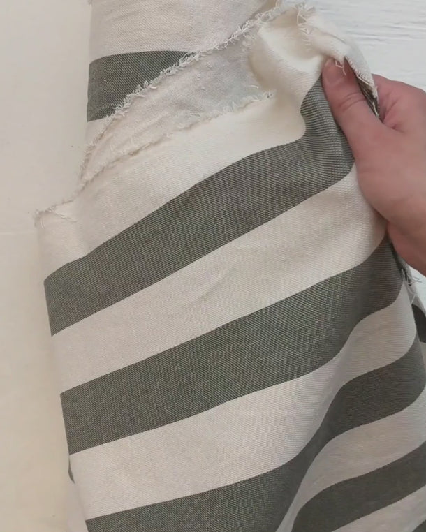 Hand som visar strukturen i det randiga tyget Filippa i grön och natur